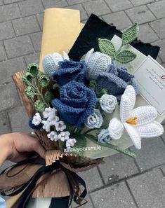 crocheted flowers are being held by someone's hand on the sidewalk in front of an envelope