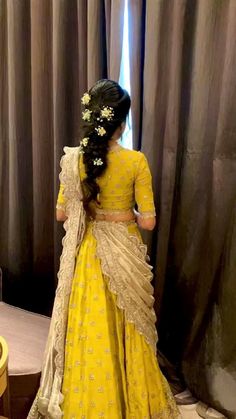 a woman standing in front of a window wearing a yellow lehenga with white flowers on it