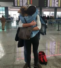 two people hugging each other in an airport with luggage on the ground and signs above them