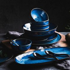 a stack of blue dishes sitting on top of a wooden cutting board next to an apple