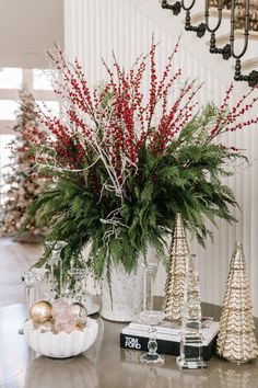 christmas decorations on a table with red berries and greenery in a white vase next to candlesticks