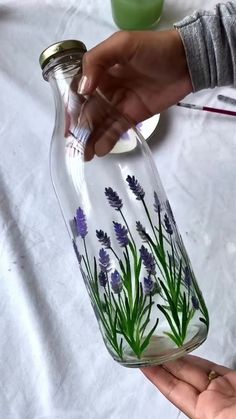 a person holding a glass jar with flowers painted on it