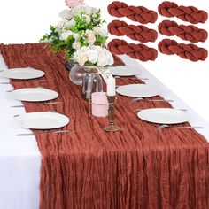 the table is set with white plates and red napkins on it, along with pink flowers