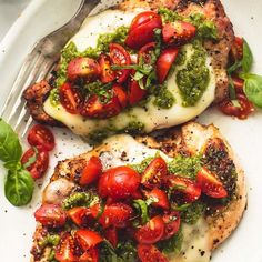 two pieces of chicken with tomatoes and pesto on top, next to a fork