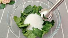 a glass bowl filled with green leaves and white sugar on top of a gray table cloth