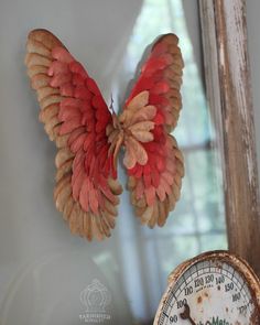 a clock with wings hanging from it's side next to a wall mounted thermometer