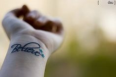 a close up of a person's wrist with the word believe tattooed on it