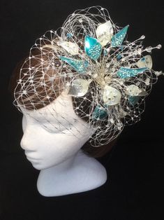 Teal blue and silver veiled fascinator perfect for the guest who wants something beautifully unique. This design is a beautiful selection of glass effect leaves and flowers clustered together amongst a fine layer of veiling and set onto a fine comfort base tiara band. As with all our designs, this piece can be made exact to the image or in any colour combination to match in with your outfit. If a specific colour is required customers can message over an image of their outfit and accessories, or Elegant Blue Headpiece With Handmade Flowers, Elegant Blue Fascinator With Handmade Flowers, Silver Costume Hats And Headpieces For Kentucky Derby Wedding, Handmade White Wedding Fascinator, Silver Mini Hat For Wedding And Kentucky Derby, Blue Handmade Flower Hair Accessories For Weddings, Silver Mini Hats For Kentucky Derby And Weddings, Blue Handmade Flower Wedding Hair Accessories, Handmade Pinched Crown Fascinator For Wedding