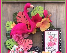 a pink flamingo wreath on a wooden wall with flowers and cards in front of it