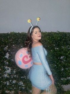 a woman in a blue dress is holding a balloon with two antennae on her head