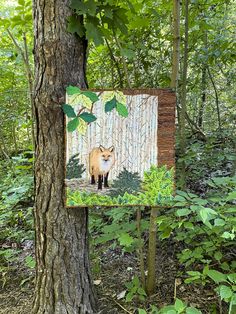 a painting of a fox is hanging on the side of a tree in the woods