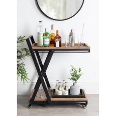 a bar cart with liquor bottles and glasses on it in front of a round mirror