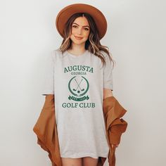 Not pictured on model: Baby Blue and Athletic Heather Get ready for The Masters in Augusta, Georgia, USA in style with our premium golf T-shirt. Made from a soft and comfortable cotton blend, this sweatshirt is perfect for both on and off the golf course or if you are watching on your couch in the comfort of your own home. With its sleek and stylish design, it's the perfect addition to any golfer's or spectator wardrobe. So whether you're heading out to the course or just looking to show off you Sporty Cotton Golf Shirt, Sporty Green Golf Shirt, Sporty Golf Tops With Logo Print, Green Letter Print T-shirt For Golf, Casual Graphic Print T-shirt For Golf, Sporty T-shirt With Team Name For Golf, Cotton Golf Shirt With Graphic Print, Green Cotton Golf T-shirt, Sporty Golf Shirt With Graphic Print