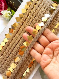 a hand is holding up some gold foiled paper with small triangles on the edge