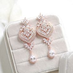 two pairs of diamond earrings sitting on top of a white velvet box with the lid open