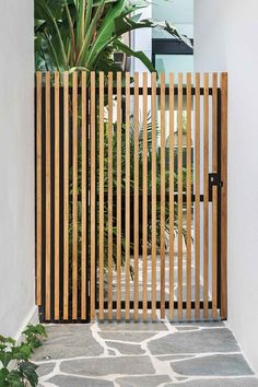 an open wooden gate on the side of a building next to a stone walkway and potted plant