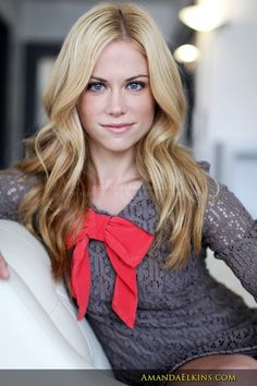 a woman with long blonde hair and a red bow on her neck smiles at the camera