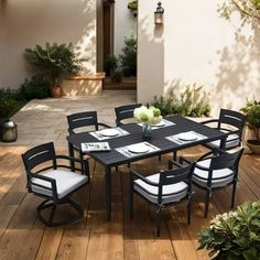 an outdoor dining table and chairs set up on a wooden deck with potted plants