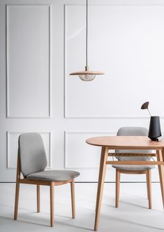 two chairs and a table in front of a white wall with a lamp hanging from the ceiling