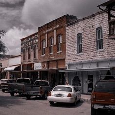 cars are parked on the street in front of stores and buildings with an american flag hanging from the roof