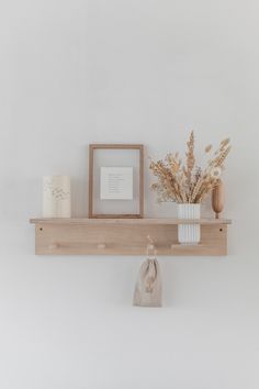 a wooden shelf with two vases on it and some pictures hanging from the wall