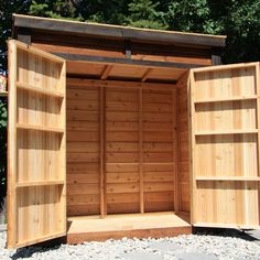 a wooden storage shed with open doors on the outside and gravel ground in front of it