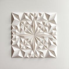 a white paper sculpture on the wall with an intricate geometric design in it's center