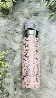 a pink insulated water bottle sitting on top of a fur covered floor next to green plants