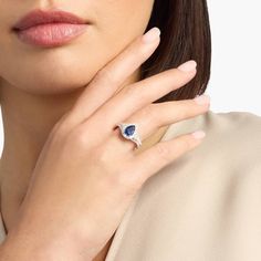 a woman with her hand on her neck wearing a blue and white diamond ring in front of her face