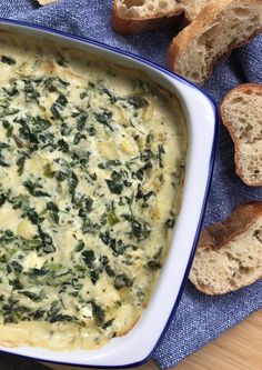 a casserole dish with spinach and cheese in it on a blue towel next to bread