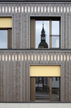 two windows with blinds on each side and a clock tower in the background