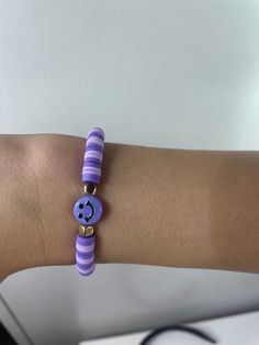 a woman's arm wearing a purple and white bracelet with a smiley face on it