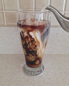 a glass filled with liquid sitting on top of a counter next to a metal spoon