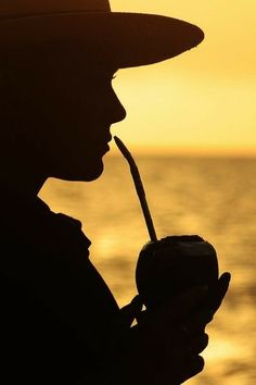 the silhouette of a man drinking from a straw in front of an ocean at sunset