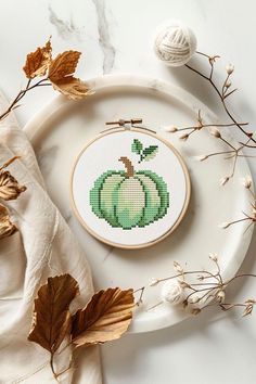 a cross stitch pumpkin on a plate next to some dried leaves