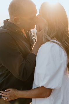 a man and woman kissing in front of the sun