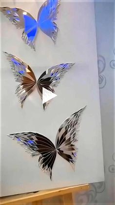 three metal butterflies on display in a glass case with blue and silver foiled wings