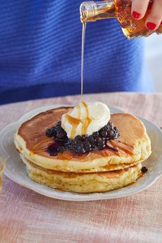 a person pouring syrup on top of some pancakes