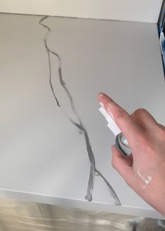 a person is drawing on a piece of paper with white paint and a brush in their hand