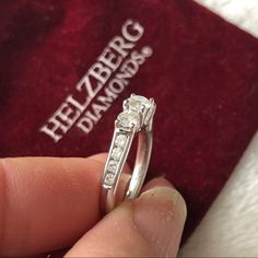 a person holding a ring in their hand with a red velvet box behind it that says helbberg diamonds