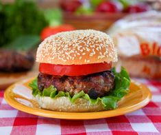 a hamburger with lettuce, tomato and cheese on a yellow plate sitting on a checkered tablecloth