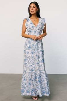 a woman wearing a blue and white floral print dress, standing in front of a wall