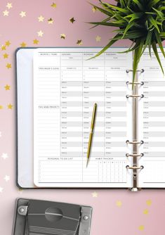 a planner and pen sitting on top of a pink desk next to a potted plant