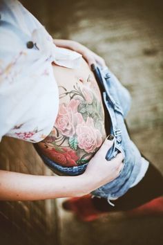 a pregnant woman is holding her stomach with flowers on it and she has tattoos on her belly