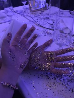 two hands covered in glitter sitting on top of a table next to glasses and silverware