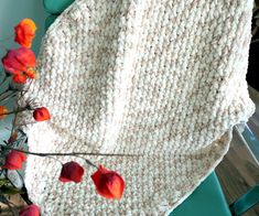 a crocheted blanket sitting on top of a green chair next to red flowers