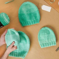 two green knitted hats sitting on top of a table next to scissors and yarn