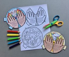 two hands and four different colored crayons on top of a piece of paper