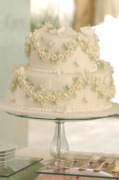 a white wedding cake sitting on top of a glass table next to plates and utensils