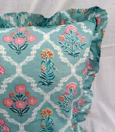 a blue pillow with pink and orange flowers on the front, sitting on a white sheet